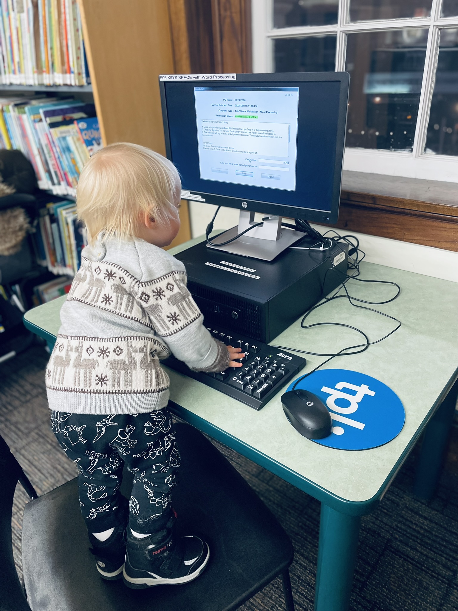 toddler standing on a chair in front of a computer at a library