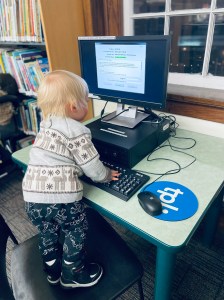 toddler standing on a chair in front of a computer at a library