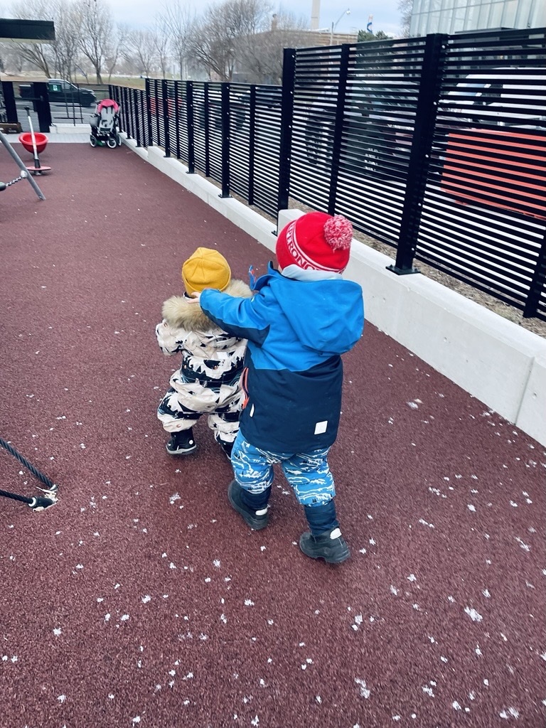 two young children wearing snowsuits chasing each other on a playground