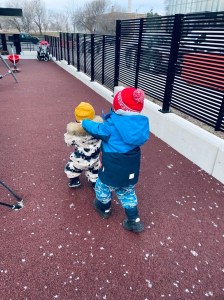 two young children wearing snowsuits chasing each other on a playground