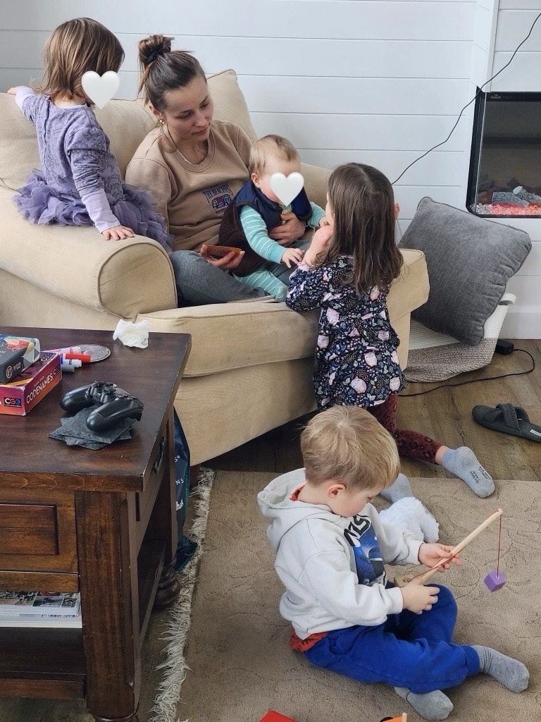 young woman sitting on an armchair with baby on lap surrounded by three young children