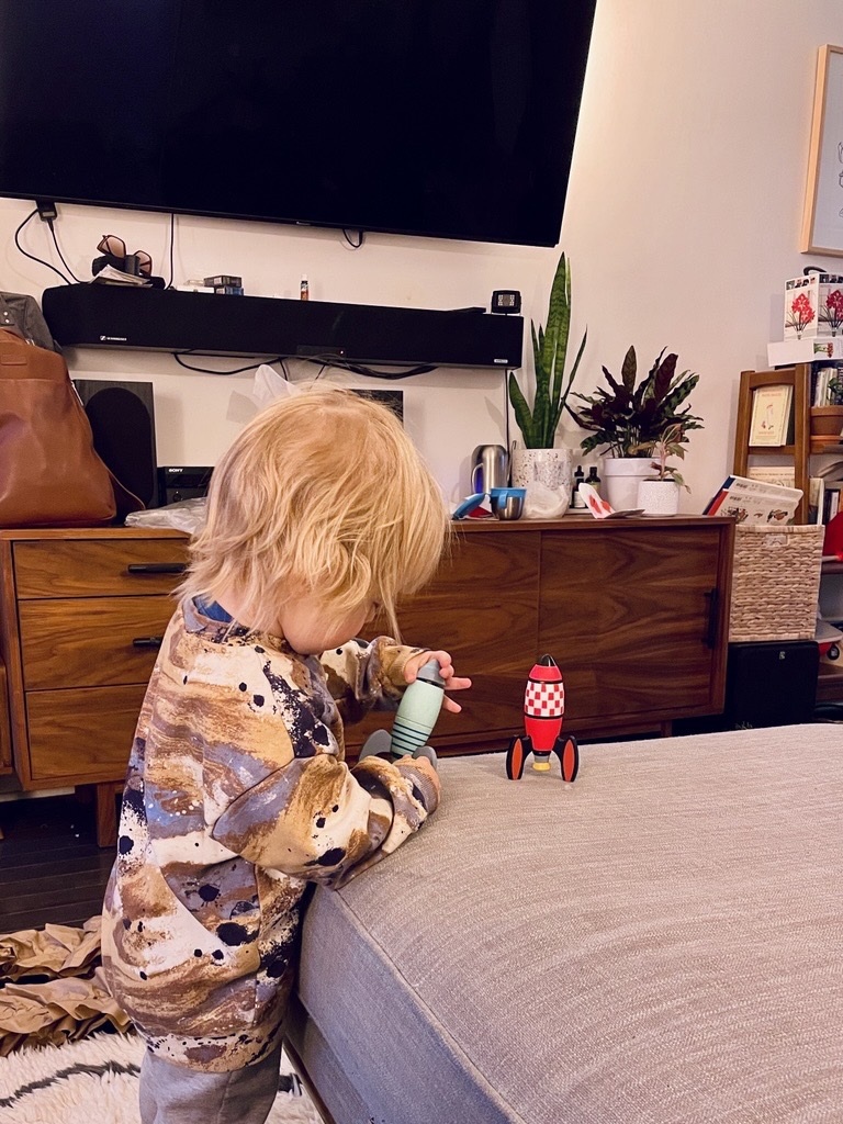 Toddler playing with space rocket toys, TV in the background